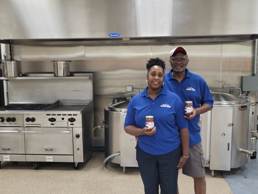 Deborah James and Freddie L. James Jr. holding jars in their Carr Street plant, beside the cooking kettles