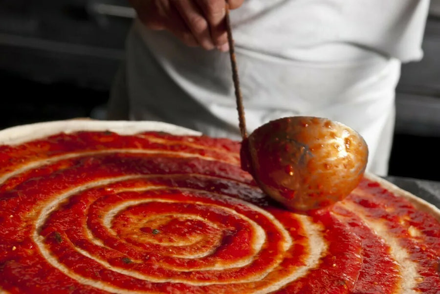 Freddie Lee's sauce being ladled in a spiral over fresh pizza dough